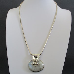 May include: A silver chain necklace with a silver pendant featuring a white moonstone. The pendant has a detailed design with swirls and a small bead.