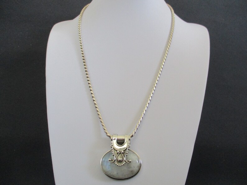 May include: A silver chain necklace with a silver pendant featuring a white moonstone. The pendant has a detailed design with swirls and a small bead.