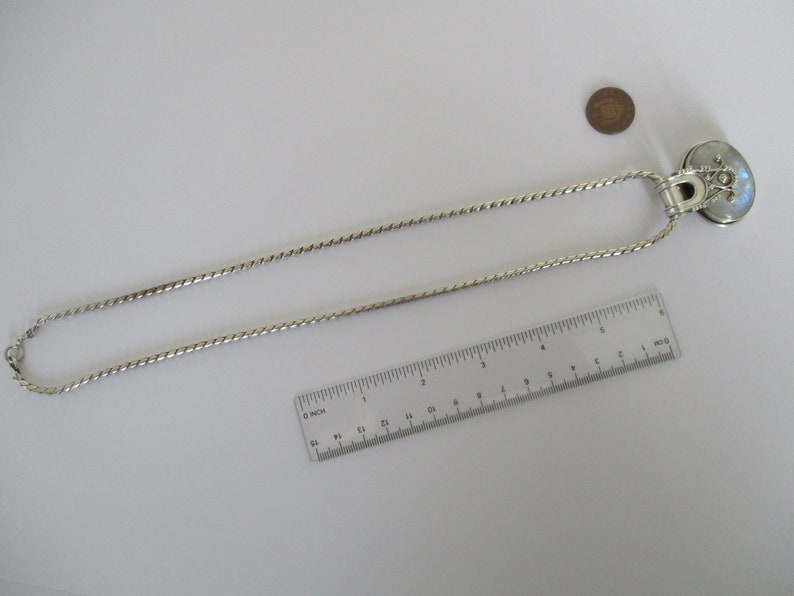 May include: A silver chain necklace with a silver pendant featuring a round, iridescent moonstone. The necklace is 18 inches long and is shown next to a ruler and a coin for size reference.