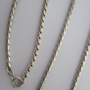 May include: A silver chain necklace with a twisted design. The chain is made of small, linked metal pieces.