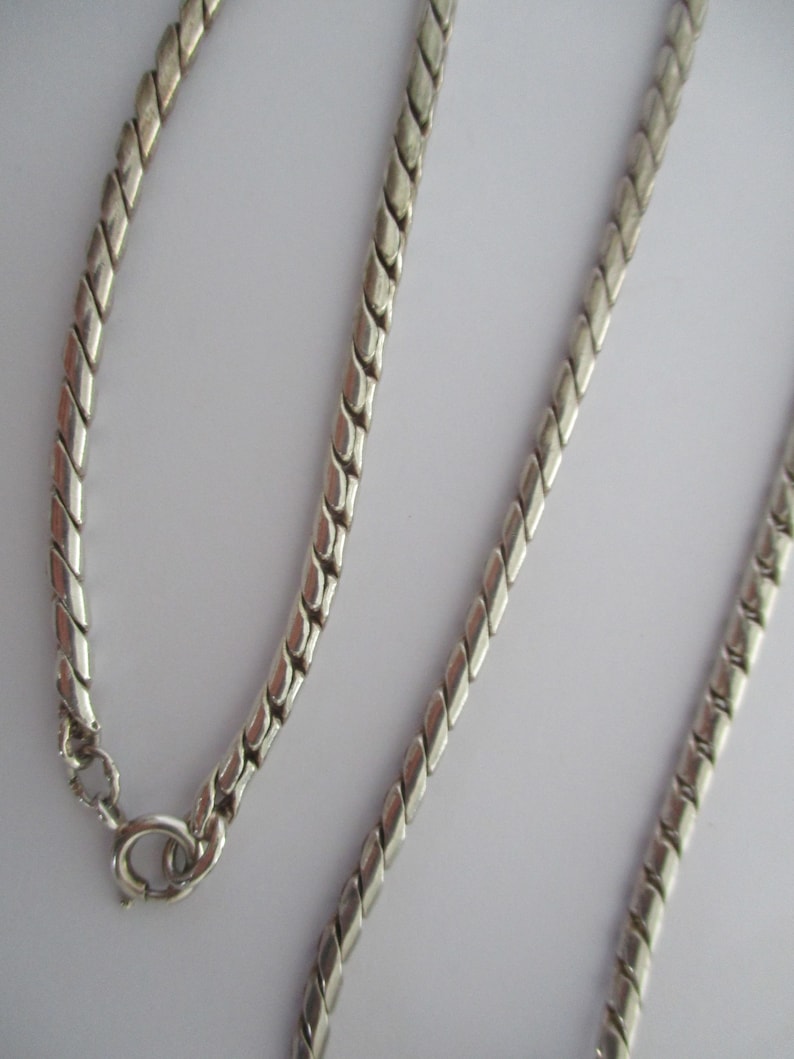 May include: A silver chain necklace with a twisted design. The chain is made of small, linked metal pieces.