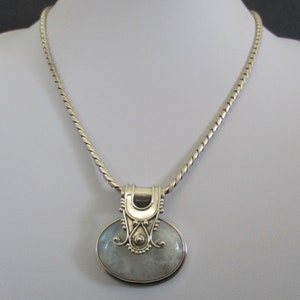 May include: A silver chain necklace with a silver pendant featuring a white moonstone. The pendant has a detailed design with a curved top and a decorative border.