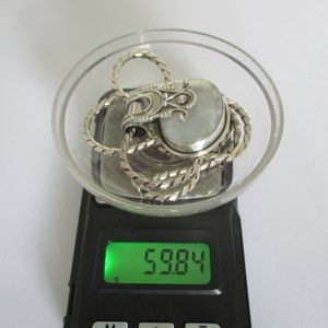 May include: A silver chain necklace with a silver pendant featuring a white stone and intricate details. The necklace and pendant are on a digital scale that reads 59.84.