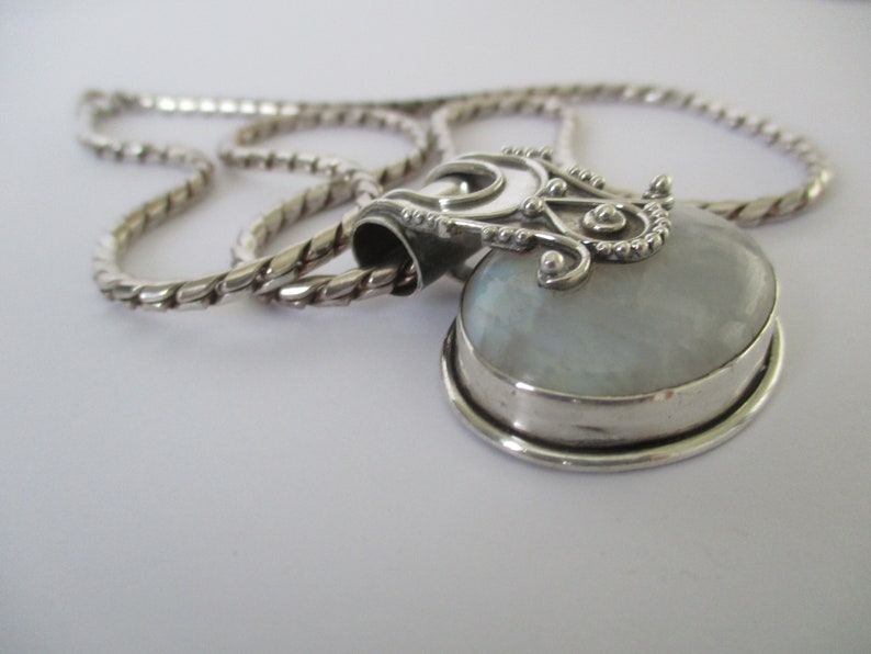 May include: A silver chain necklace with a heart-shaped pendant featuring a white iridescent stone.