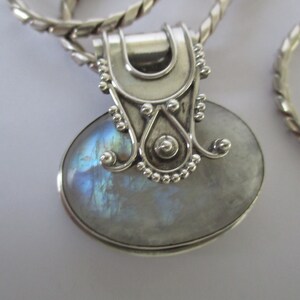 May include: A silver pendant with a large oval moonstone set in a silver bezel. The pendant has a detailed silver bail with a decorative design.
