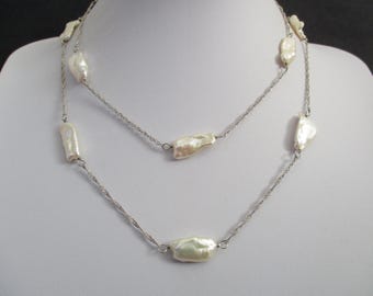 May include: A two-strand necklace featuring irregularly shaped, off-white pearls strung on a delicate silver chain. The necklace is displayed on a white mannequin, showcasing its elegant design and natural pearl texture.