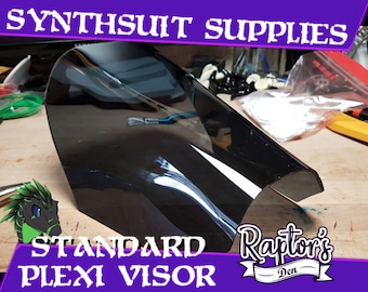 May include: A clear, dark gray plastic visor for a synthsuit. The visor is curved and has a rounded edge. The text "STANDARD PLEXI VISOR" is printed in white on a purple background. The text "Raptor's Den" is printed in white on a purple background with a white ribbon.