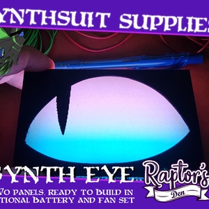Può includere: Due pannelli neri con un design a occhio sfumato blu, rosa e bianco. I pannelli sono per costruire un occhio sintetico, e il testo "SYNTH EYE Raptor's Den" è stampato sotto l'occhio. Il testo "TWO PANELS, READY TO BUILD IN OPTIONAL BATTERY AND FAN SET" è stampato sotto il logo.