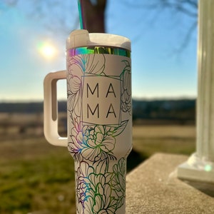 May include: White travel mug with a floral design and the word "MAMA" in a square on the front. The mug has a handle and a lid with a straw.