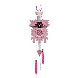 Könnte beinhalten: Eine rosa Kuckucksuhr mit einem Hirschkopf und Geweih. Die Uhr hat ein florales Design, ein kreisförmiges Zifferblatt und zwei rosa, zapfenförmige Gewichte, die an Ketten hängen. Der Hirschkopf ist weiß mit rosa Geweih.