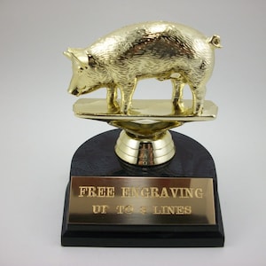 May include: Gold-colored pig trophy with a black base. The base has a gold-colored plate with the text "FREE ENGRAVING UP TO 4 LINES".