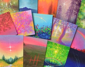 May include: A collection of colorful art prints featuring landscape scenes. The prints showcase various natural elements, including trees, fields, and skies, with vibrant colors and artistic details. The artwork is displayed on a blue surface.