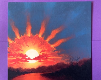 May include: A square print of a sunset over a river. The sun is a bright white orb surrounded by red and orange clouds. The sky is a deep blue, and the river reflects the sunset's colors. Bare trees line the riverbank.