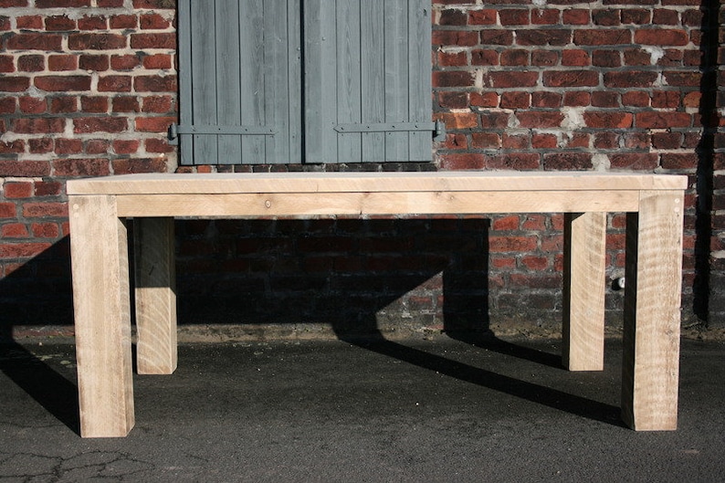 K&ouml;nnte beinhalten: Ein heller Holz-Esstisch mit rechteckiger Tischplatte und vier Beinen. Der Tisch steht vor einer Backsteinwand mit einem geschlossenen Fensterladen.