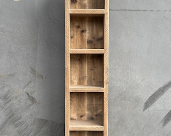 Puede incluir: Una estantería alta y estrecha de madera con cinco estantes. La estantería está hecha de madera clara sin terminar, mostrando la veta natural y los nudos. El diseño es simple y rústico, adecuado para varios estilos de decoración.