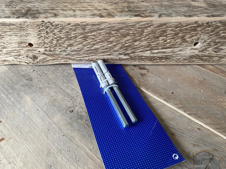 May include: Two silver metal drywall anchors packaged on a blue background with white polka dots. The anchors are used for hanging heavy objects on drywall.