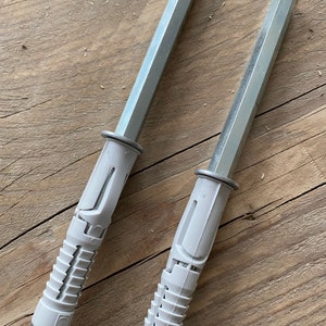 May include: Two silver and white plastic drywall anchors with a hexagonal head. The anchors are designed to be used with screws to secure objects to drywall.