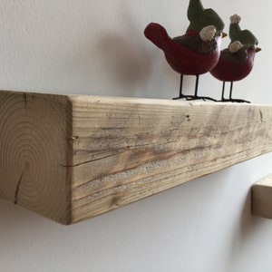 May include: A rustic wooden shelf with a natural finish. The shelf is made from reclaimed wood and has a unique, weathered look. Two small red birds with green hats are perched on the shelf.