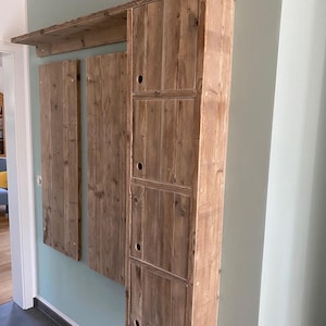 Könnte beinhalten: Ein an der Wand montierter Holzschrank mit vier Türen und einem Regal darüber. Der Schrank ist aus recyceltem Holz gefertigt und hat eine rustikale Oberfläche.
