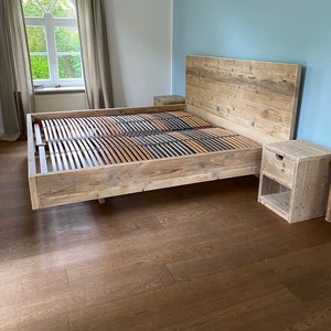 Könnte beinhalten: Ein rustikaler Holzbettenrahmen mit passendem Kopfteil und zwei Nachttischen. Der Bettrahmen hat eine Lattenrostbasis und ist aus hellfarbigem Holz gefertigt. Der Raum hat eine blaue Wand und ein Fenster mit Vorhängen.