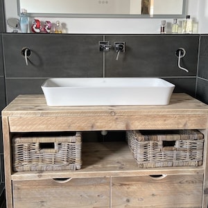 May include: A rustic wooden bathroom vanity with two drawers and two wicker baskets. The vanity has a white porcelain sink and a chrome faucet.