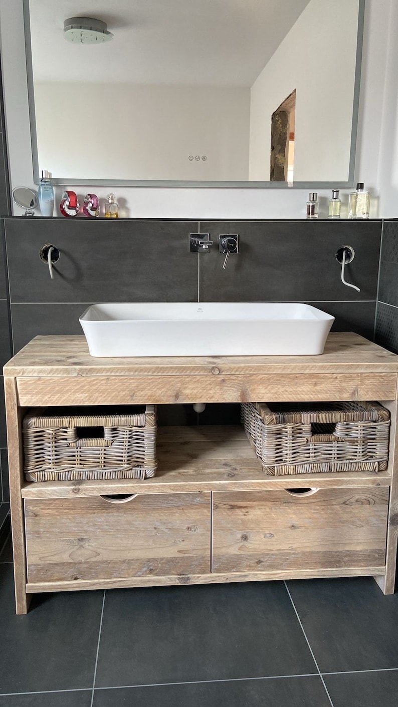 May include: A rustic wooden bathroom vanity with two drawers and two wicker baskets. The vanity has a white porcelain sink and a chrome faucet.
