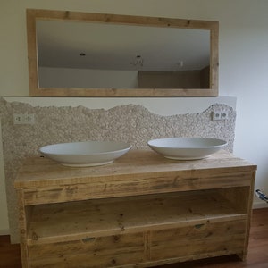 May include: A double vanity bathroom sink with two white porcelain sinks, a wooden countertop, and two drawers. The vanity is made of reclaimed wood and has a rustic look. The backsplash is made of small white tiles.
