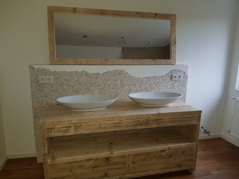 May include: A double vanity bathroom sink with two white porcelain sinks, a wooden countertop, and two drawers. The vanity is made of reclaimed wood and has a rustic look. The backsplash is made of small white tiles.