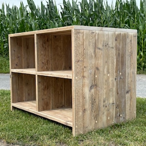 Könnte beinhalten: Ein rustikales Holzregal mit vier offenen Fächern. Das Regal ist aus recyceltem Holz mit einer natürlichen Oberfläche und hat einen leicht abgenutzten Look. Das Regal steht auf einem Bett aus grünem Gras.