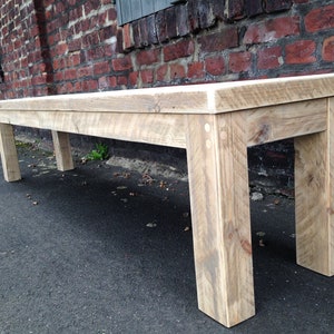 Puede incluir: Un banco de madera r&uacute;stico largo con un acabado natural envejecido. El banco tiene un dise&ntilde;o sencillo con cuatro patas y una parte superior ancha y plana. El banco est&aacute; hecho de madera recuperada y tiene un aspecto r&uacute;stico natural.