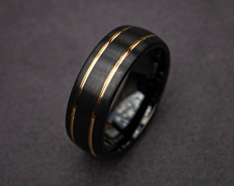 Könnte beinhalten: Ein schwarzer Ring aus Wolframcarbid mit zwei goldenen Bändern um die Mitte.