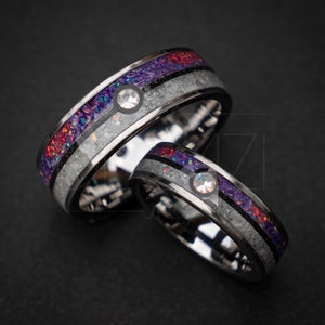 Puede incluir: Dos anillos de plata con una incrustación negra y una incrustación de ópalo púrpura y blanco. Cada anillo tiene una pequeña piedra transparente engastada en la incrustación.