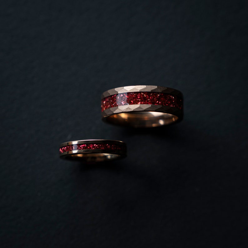 K&ouml;nnte beinhalten: Zwei goldene Ringe mit roter Einlage. Die Ringe liegen auf einem schwarzen Hintergrund.