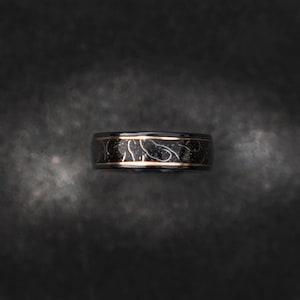 May include: A black and gold ring with a decorative pattern. The ring is made of metal and has a polished finish.