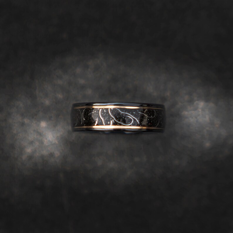 May include: A black and gold ring with a decorative pattern. The ring is made of metal and has a polished finish.