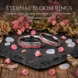Puede incluir: Dos anillos de tungsteno en tono plateado con una incrustación de flores secas rosas y material gris. El texto ETERNAL BLOOM RINGS, Tungsten Silver, Rainbow Moonstone, Pink Dried Flowers, Handcrafted & Unique es visible arriba.