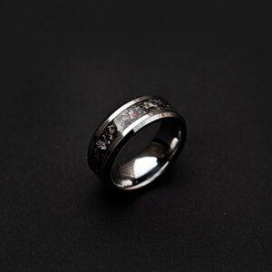 May include: A silver ring with a black and red inlay. The ring has a beveled edge and a polished finish.