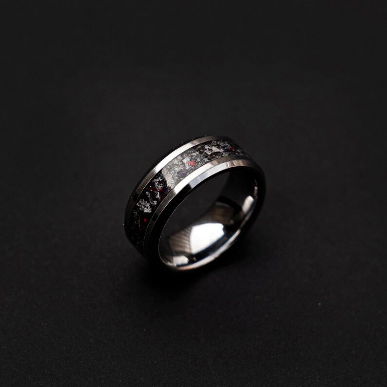 May include: A silver ring with a black and red inlay. The ring has a beveled edge and a polished finish.
