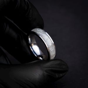 Op de afbeelding: Een zilveren ring met een witte inlay. De ring is gemaakt van roestvrij staal en heeft een gepolijste afwerking.