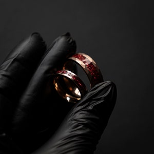 K&ouml;nnte beinhalten: Zwei Ringe aus Ros&eacute;gold mit einer roten Glitzer-Einlage. Die Ringe sind &uuml;bereinander gestapelt.