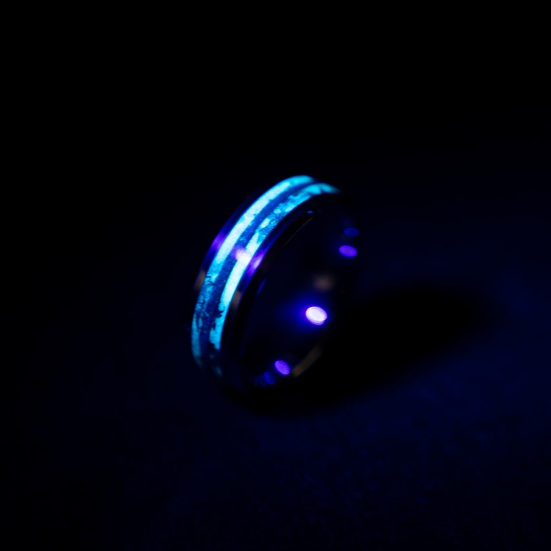 May include: A black ring with two glowing blue stripes. The ring is made of metal and has a smooth finish.