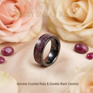 Puede incluir: Un anillo de cerámica negra con una incrustación de rubí triturado. El texto RUBY INLAY RING aparece en la parte superior y el texto Genuine Crushed Ruby & Durable Black Ceramic se encuentra en la parte inferior.