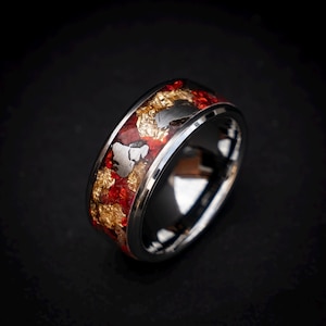 以下が含まれることがあります： 赤と金のインレイが施された銀の指輪。インレイは、銀のバンドに埋め込まれた小さな赤と金の素材でできています。指輪はシンプルなデザインですが、インレイがユニークで目を引くものになっています。