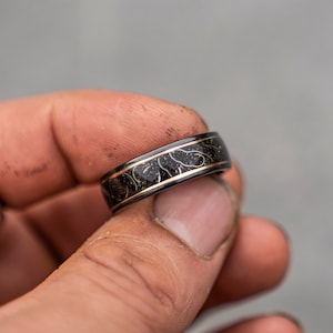 May include: A black and gold ring with a decorative pattern. The ring is made of metal and has a polished finish.