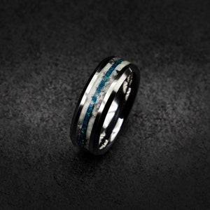 May include: A black tungsten carbide ring with a white and blue inlay. The inlay is made of opal and has a speckled pattern.