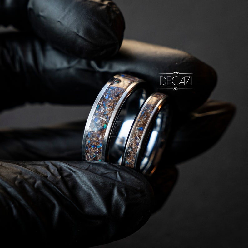 May include: Two silver rings with a brown and blue speckled inlay. The rings are shown together in a black gloved hand. The text "DECAZI" is visible in the background.