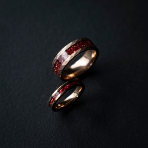 K&ouml;nnte beinhalten: Zwei goldene Ringe mit einem roten Edelstein-Inlay. Die Ringe sind &uuml;bereinander gestapelt.