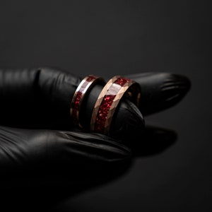 K&ouml;nnte beinhalten: Zwei goldene Eheringe mit roter Einlage. Die Ringe sind &uuml;bereinander gestapelt.