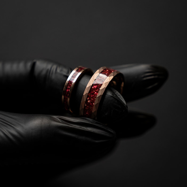K&ouml;nnte beinhalten: Zwei goldene Eheringe mit roter Einlage. Die Ringe sind &uuml;bereinander gestapelt.