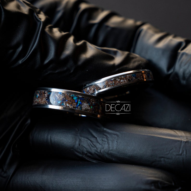 May include: Two silver rings with a brown and blue inlay. The rings are on a black surface. The text "DECAZI" is visible in the image.